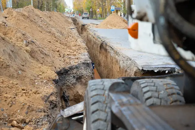 Excavator beside a long trench dug for a water pipe