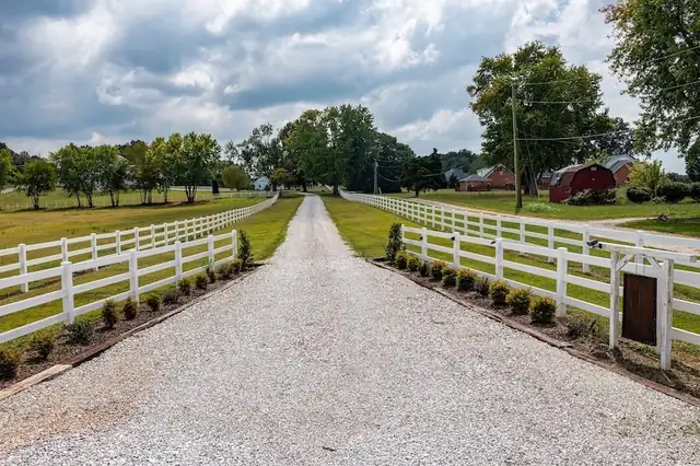 Gravel driveway lined with a white picket fence and boxwoods